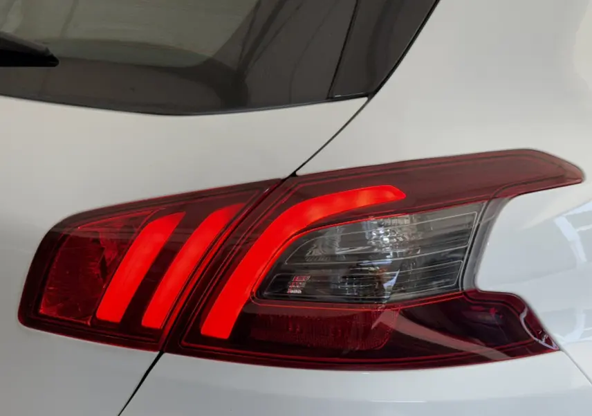 Feu arrière droit allumé d'une Peugeot 308 blanche, mettant en valeur ses lignes LED caractéristiques.