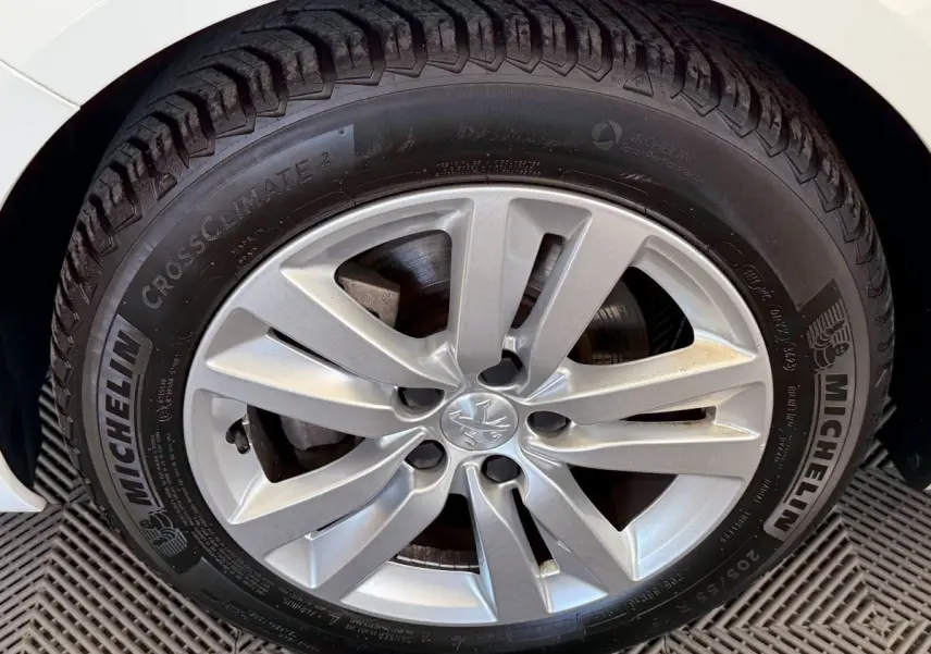 Gros plan sur la roue avant gauche d'une Peugeot 308 blanche, mettant en valeur la jante alliage et le pneu Michelin.