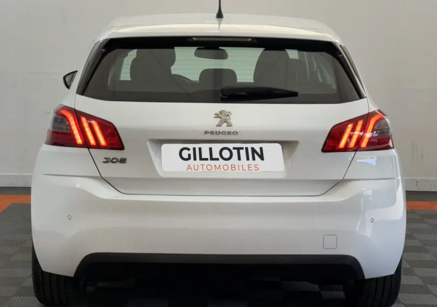 Vue arrière d'une Peugeot 308 blanche de 2021 avec feux arrière allumés et logo Peugeot visible.