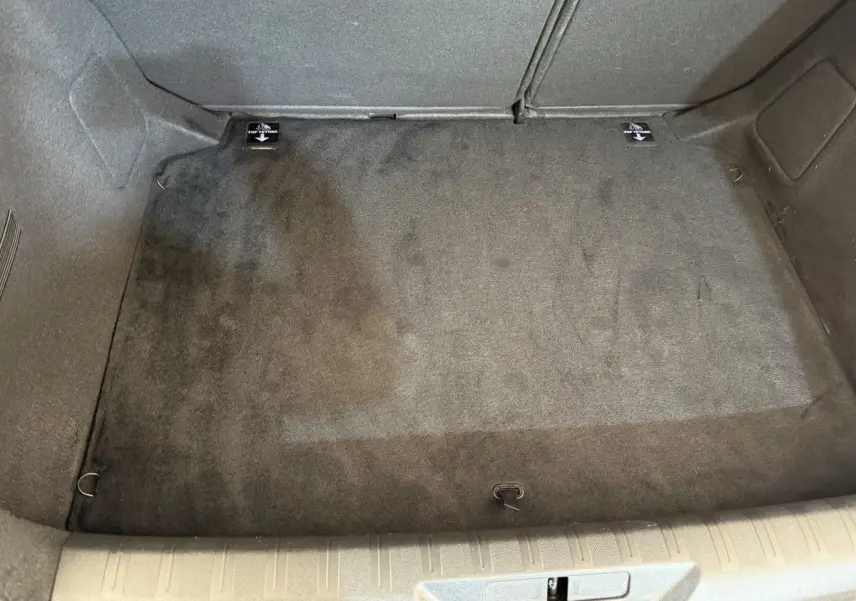 Coffre vide en vue plongeante d'une Peugeot 308 blanche, tapis de sol gris foncé et crochets d'arrimage visibles.