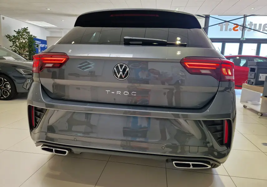 Vue arrière d'un Volkswagen T-Roc gris Indium Metal 2025 avec feux LED allumés et double sortie d'échappement rectangulaire.
