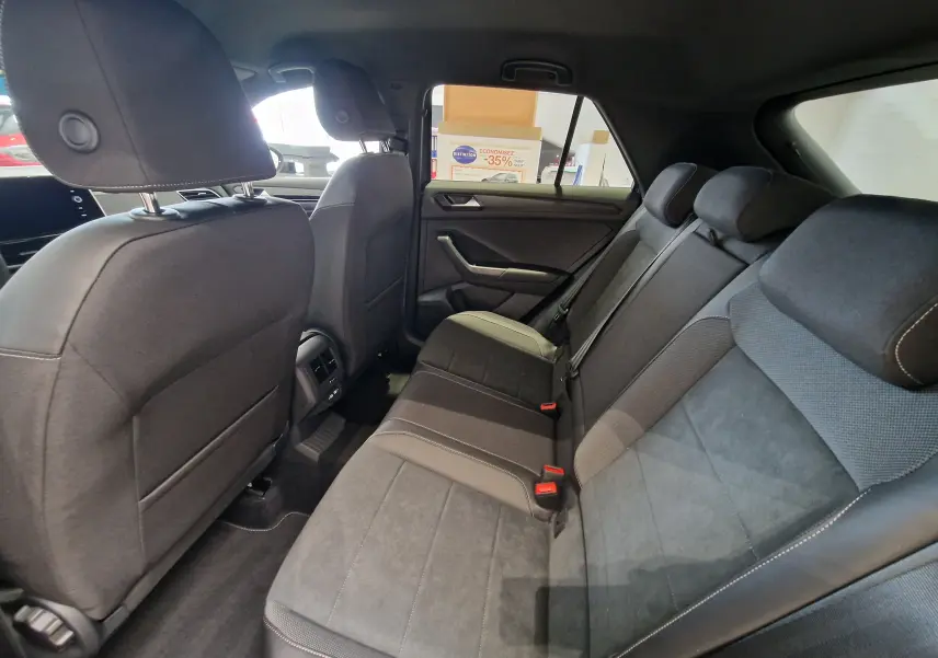 Vue intérieure arrière du Volkswagen T-Roc 2025, sièges arrière en tissu noir avec surpiqûres contrastées, ambiance sobre.