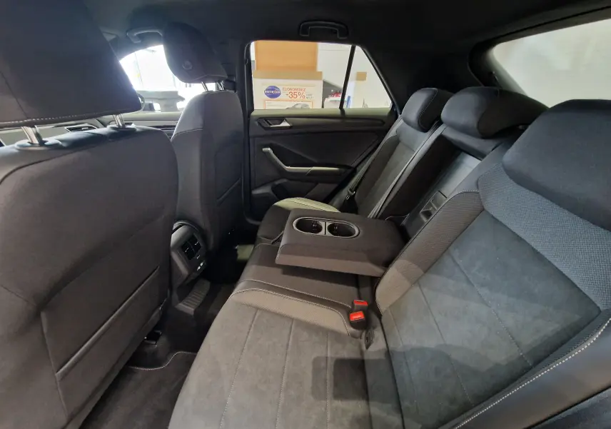 Vue intérieure arrière du Volkswagen T-Roc 2025, sièges en tissu noir avec accoudoir central et porte-gobelets intégrés.