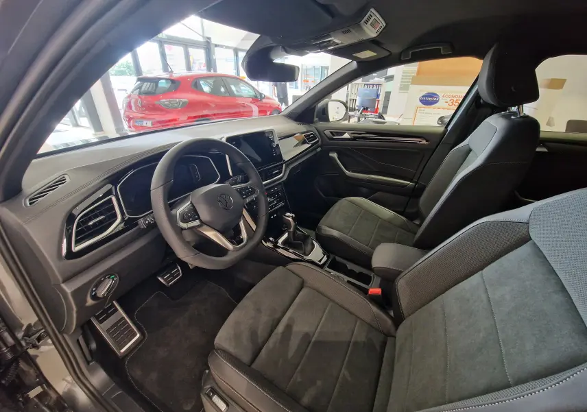 Intérieur du Volkswagen T-Roc 2025 vu côté conducteur, sièges noirs en tissu et tableau de bord moderne avec écran tactile.