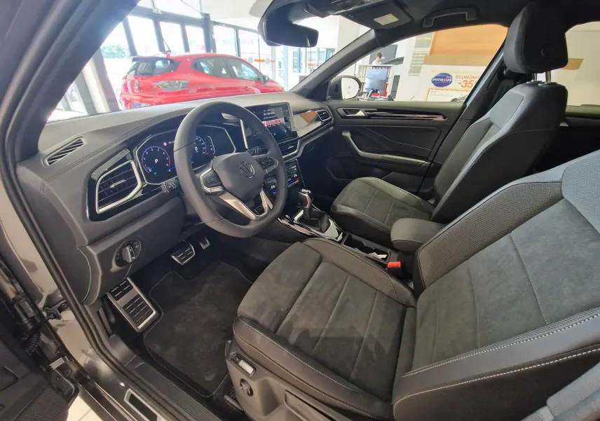 Intérieur du Volkswagen T-Roc 2025 gris Indium, vue côté conducteur montrant sièges en tissu noir et tableau de bord digital.