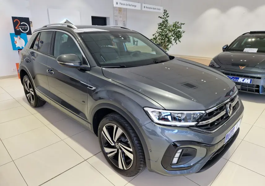 Volkswagen T-Roc gris Indium métal en 3/4 avant droit, avec jantes R-Line et calandre chromée en showroom.