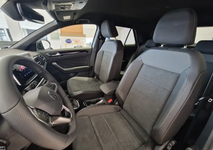 Vue intérieure côté conducteur du Volkswagen T-Roc 2025, sièges tissu noir et tableau de bord moderne.