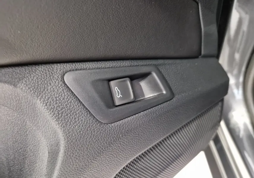 Bouton d'ouverture du coffre sur la portière intérieure droite du Volkswagen T-Roc gris Indium Metal 2025.