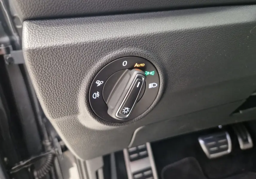 Gros plan sur le bouton de commande des phares du Volkswagen T-Roc 2025, entouré de plastique noir texturé.