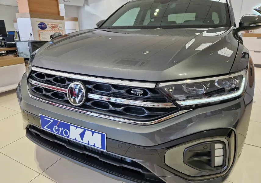 Vue de face rapprochée du Volkswagen T-Roc gris Indium Metal avec calandre R-Line et phares LED allumés en showroom.
