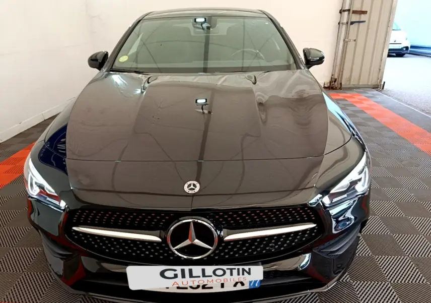Vue frontale d'une Mercedes CLA 200 d AMG Line noire avec calandre étoilée et phares LED allumés dans un garage.