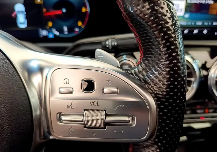 Gros plan sur la commande de volume en aluminium et cuir perforé du volant à droite d'une Mercedes CLA 200 d AMG Line noire.