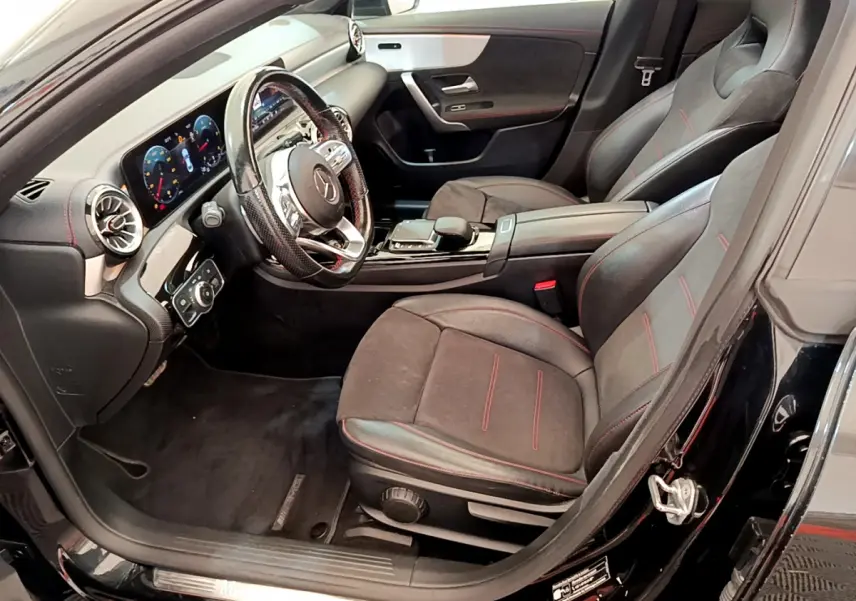 Intérieur avant droit de la Mercedes CLA 200 d AMG Line 2021 noir, sièges sport avec surpiqûres rouges et tableau de bord digital.