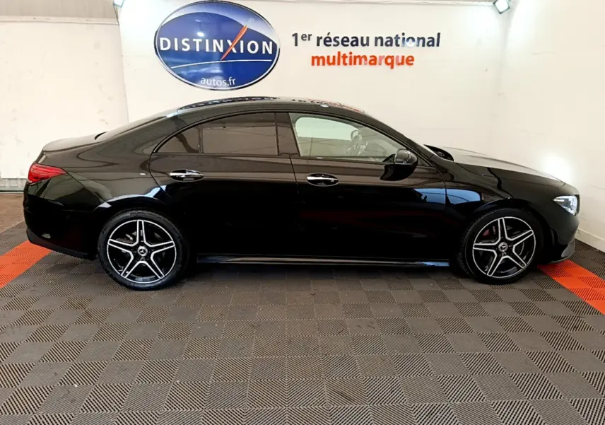 Profil côté gauche d'une Mercedes CLA 200 d AMG Line noire, avec jantes alliage et vitres teintées, en intérieur showroom.
