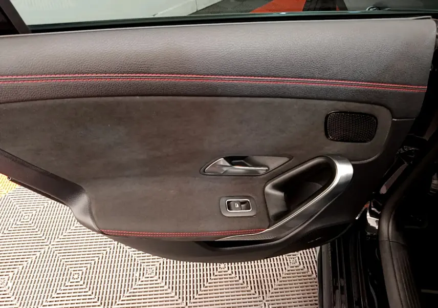Gros plan sur la porte intérieure côté gauche noire avec surpiqûres rouges et poignée métal d'une Mercedes CLA 200 d AMG Line 2021.