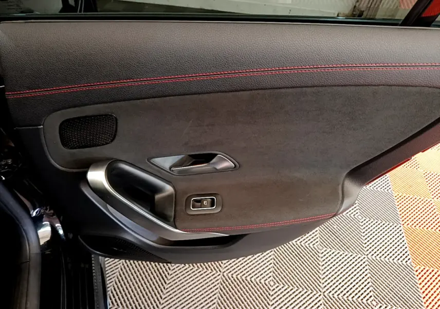 Gros plan sur la porte intérieure côté gauche d'une Mercedes CLA 200 d AMG Line noire avec surpiqûres rouges.