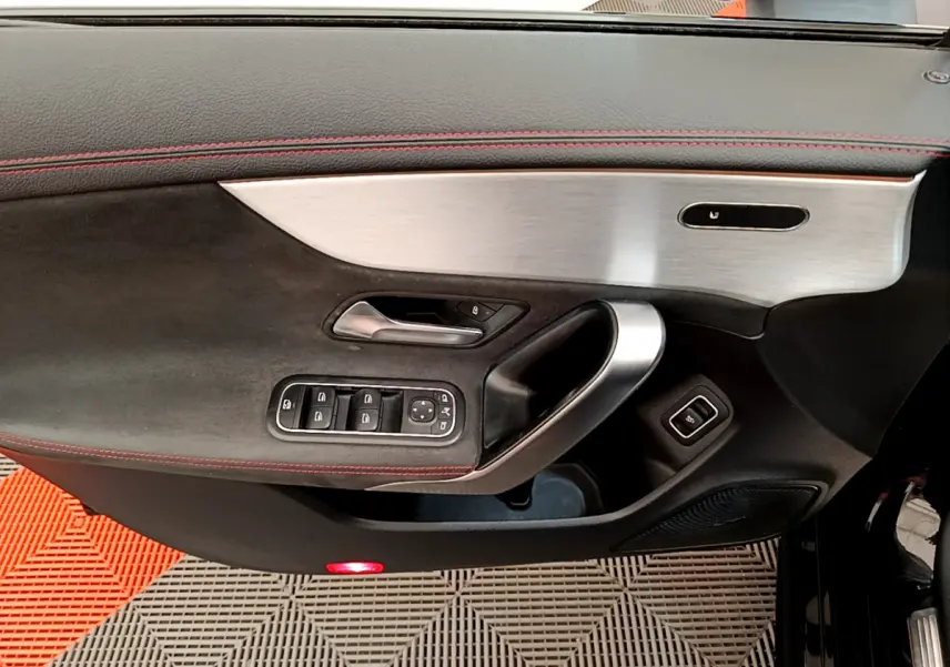Vue rapprochée de la porte côté gauche noire avec surpiqûres rouges et insert aluminium de la Mercedes CLA 200 d AMG Line 2021.