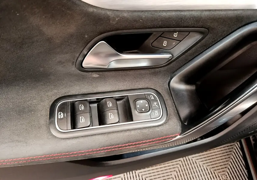 Gros plan sur la garniture intérieure noire de la porte côté conducteur avec commandes de vitres et poignée alu.