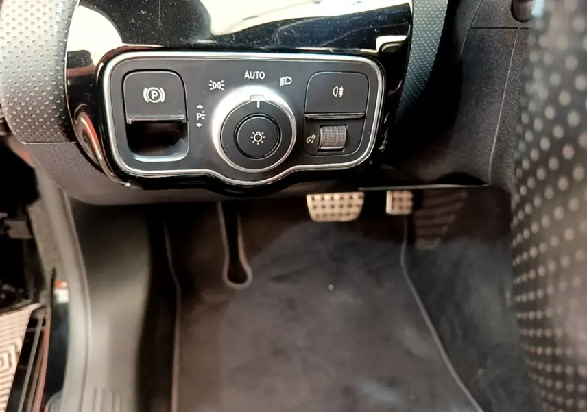 Vue rapprochée du panneau de commande des phares et frein à main électrique côté gauche d'une Mercedes CLA 200 d AMG Line noire.