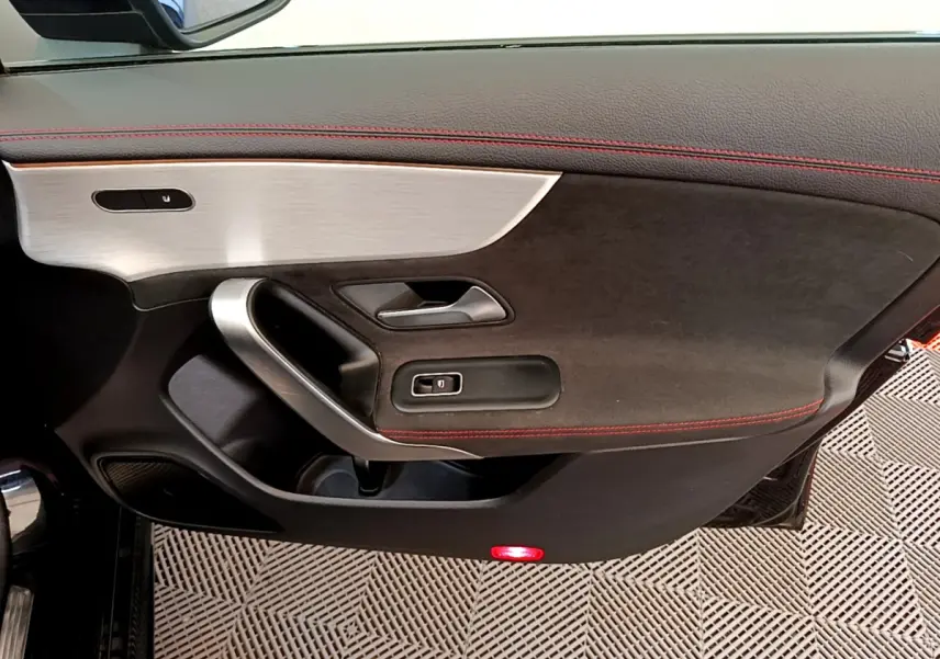 Gros plan sur la porte intérieure côté gauche de la Mercedes CLA 200 d AMG Line noire avec surpiqûres rouges et insert aluminium.