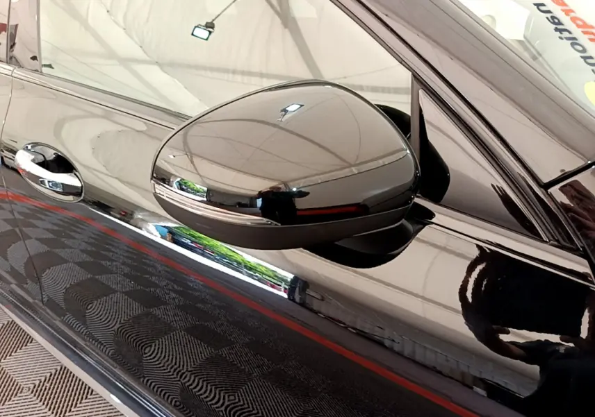 Gros plan sur le rétroviseur côté gauche noir brillant d'une Mercedes CLA 200 d AMG Line 2021 avec reflet du plafond.