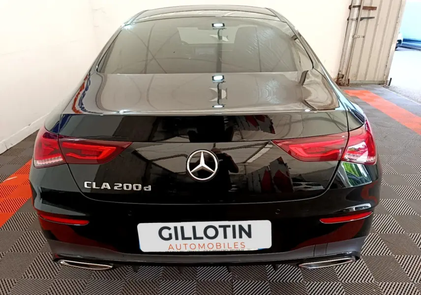 Vue arrière d'une Mercedes CLA 200 d AMG Line noire stationnée dans un garage avec feux LED allumés.