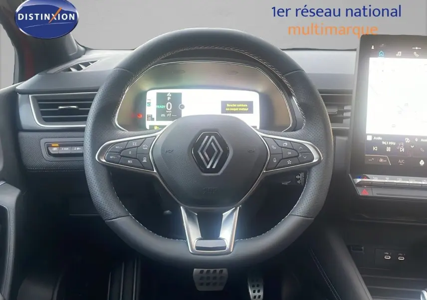 Vue intérieure centrée sur le volant noir perforé du Renault Captur E-Tech Hybrid 2025 avec tableau de bord digital et écran tactile.