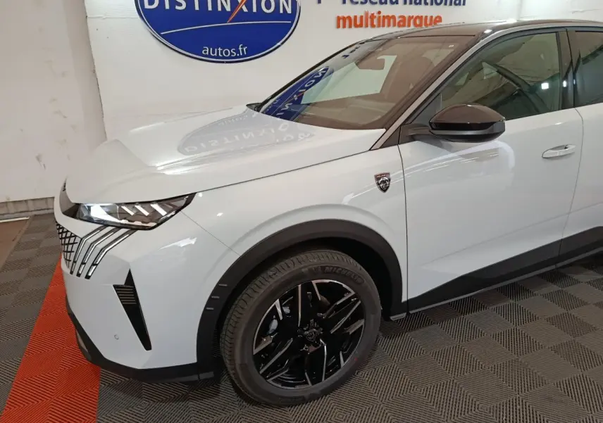 Vue 3/4 avant droit d'un Peugeot 3008 blanc avec jantes noires et calandre distinctive en intérieur showroom