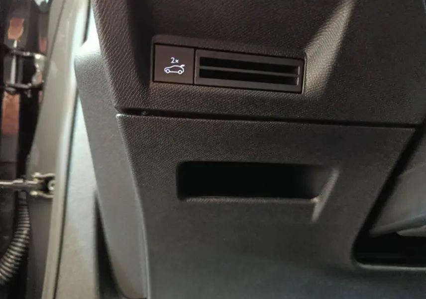 Gros plan sur le bouton d'ouverture électrique du coffre dans l'habitacle noir du Peugeot 3008 hybride blanc 2025.