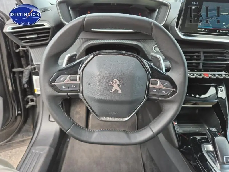 Vue rapprochée du volant multifonction noir de la Peugeot 2008 2021 avec tableau de bord numérique en arrière-plan.