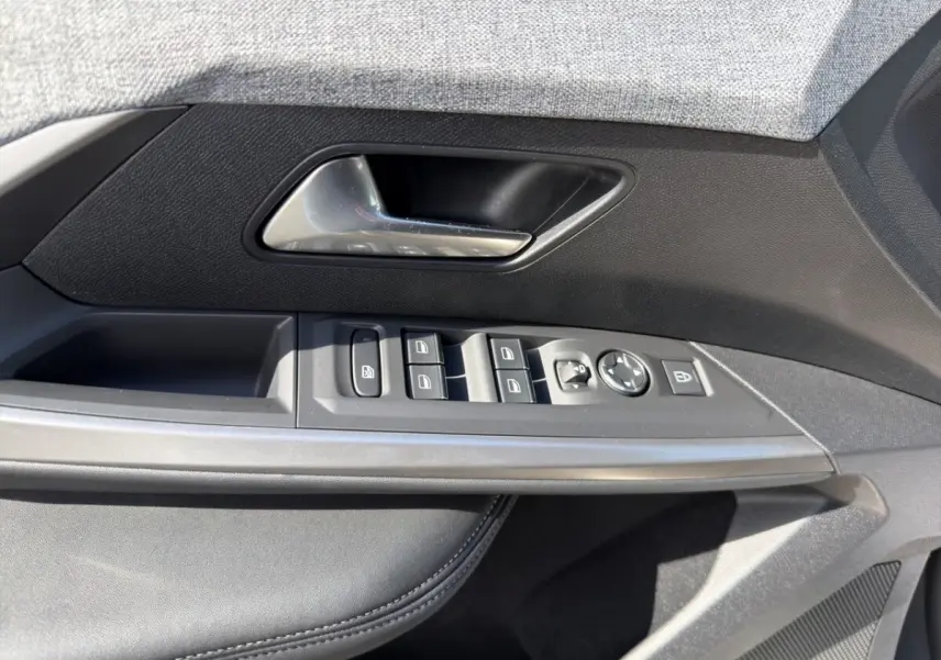 Gros plan sur la porte avant gauche du Peugeot 5008 gris foncé, montrant les commandes électriques des vitres et rétroviseurs.