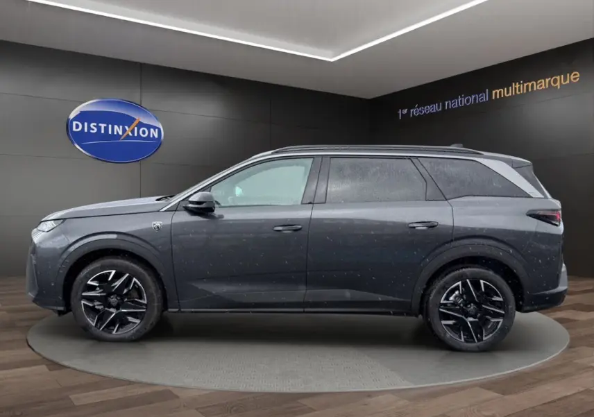 Vue latérale droite d’un Peugeot 5008 gris foncé avec jantes noires et toit surélevé en showroom.