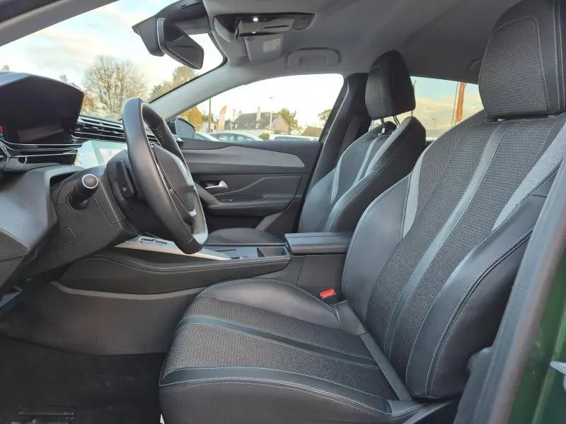 Intérieur avant de la Peugeot 308 2023 avec sièges noirs en tissu et cuir, volant multifonction et tableau de bord moderne.