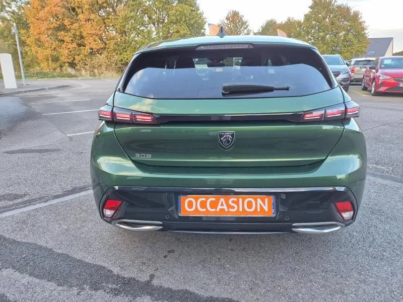 Vue arrière d'une Peugeot 308 2023 vert olivine avec feux LED et plaque orange "OCCASION" visible sur un parking.