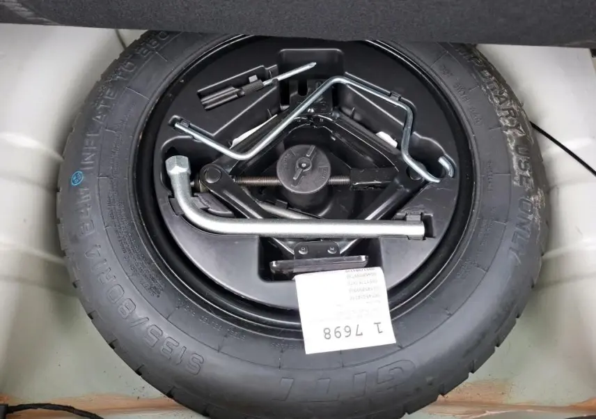 Vue plongeante sur la roue de secours noire avec outils de changement, dans le coffre d'une FIAT 500 blanche 2022.