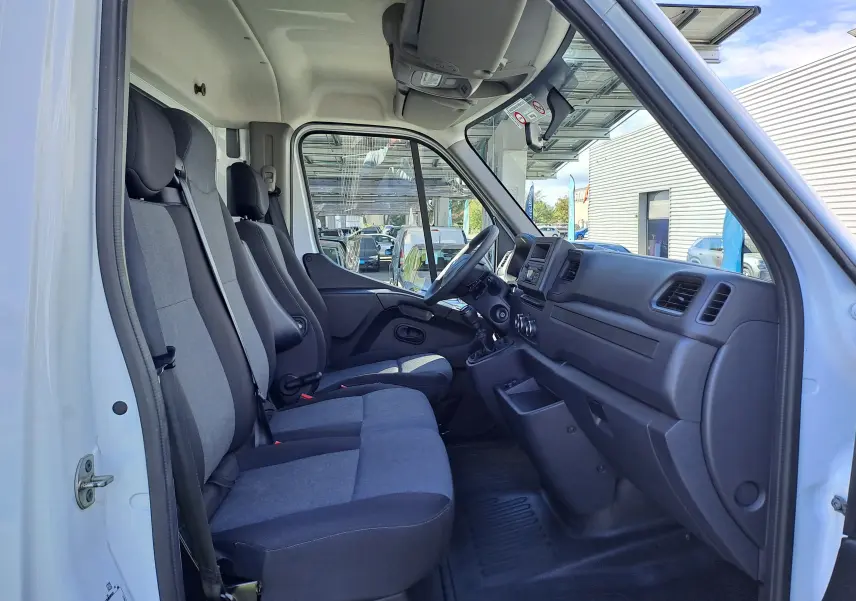 Vue intérieure côté conducteur du Nissan Interstar blanc 2024, montrant les sièges gris et le tableau de bord fonctionnel.