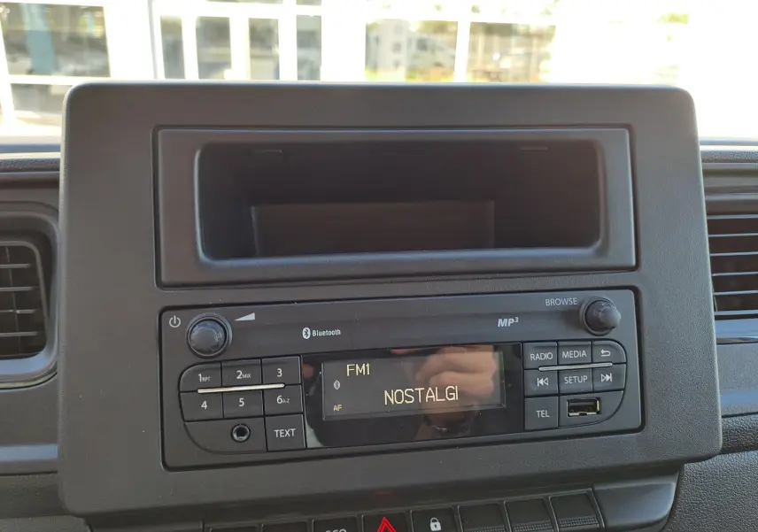 Vue rapprochée de la radio Bluetooth noire intégrée au tableau de bord du Nissan Interstar blanc, affichant la station FM1 NOSTALGI.