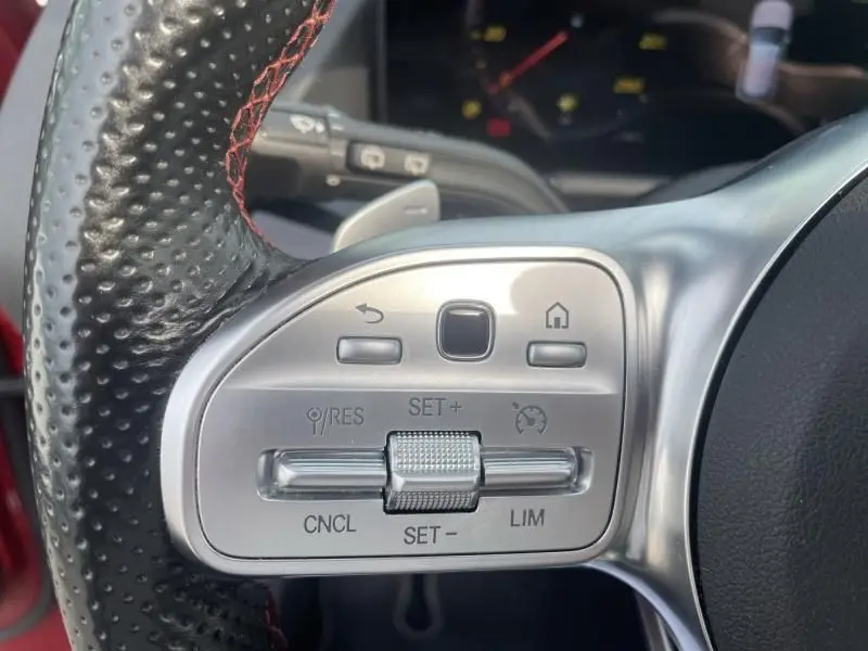 Gros plan sur les commandes du volant perforé avec surpiqûres rouges du Mercedes GLA 200 D AMG-LINE rouge métal 2022.