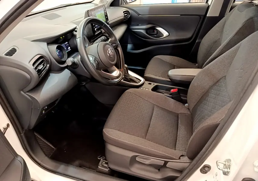 Vue intérieure côté conducteur du Toyota Yaris Cross 2022 blanc, avec sièges tissu gris et tableau de bord moderne.