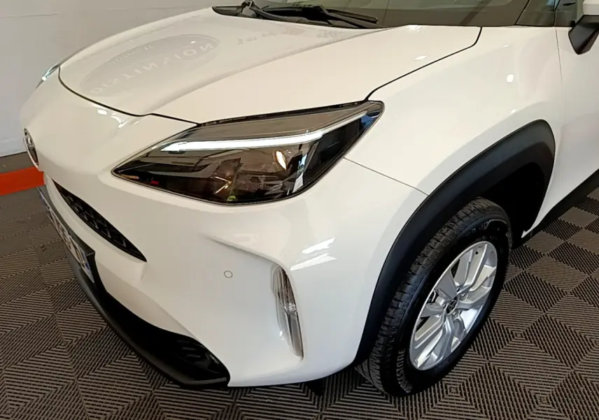 Vue 3/4 avant droit d'une Toyota Yaris Cross blanche avec phares LED et protections noires sur les passages de roues.