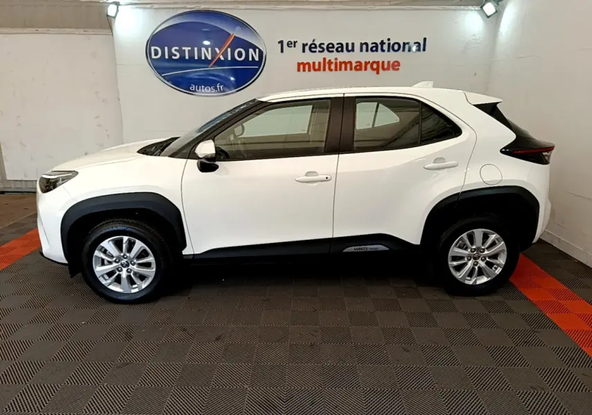 Profil droit d'une Toyota Yaris Cross blanche 2022 avec protections noires et jantes alliage visibles en intérieur showroom.