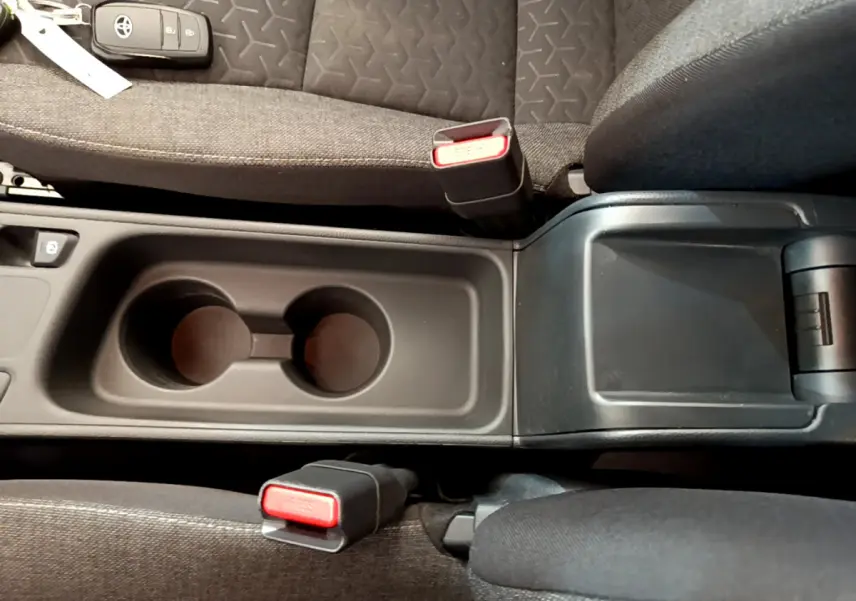 Vue plongeante sur la console centrale noire avec porte-gobelets et sièges tissu gris de la Toyota Yaris Cross blanche hybride 2022.