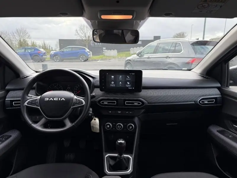 Vue intérieure avant du Dacia Jogger gris 2025, tableau de bord avec écran tactile et boîte manuelle visible.