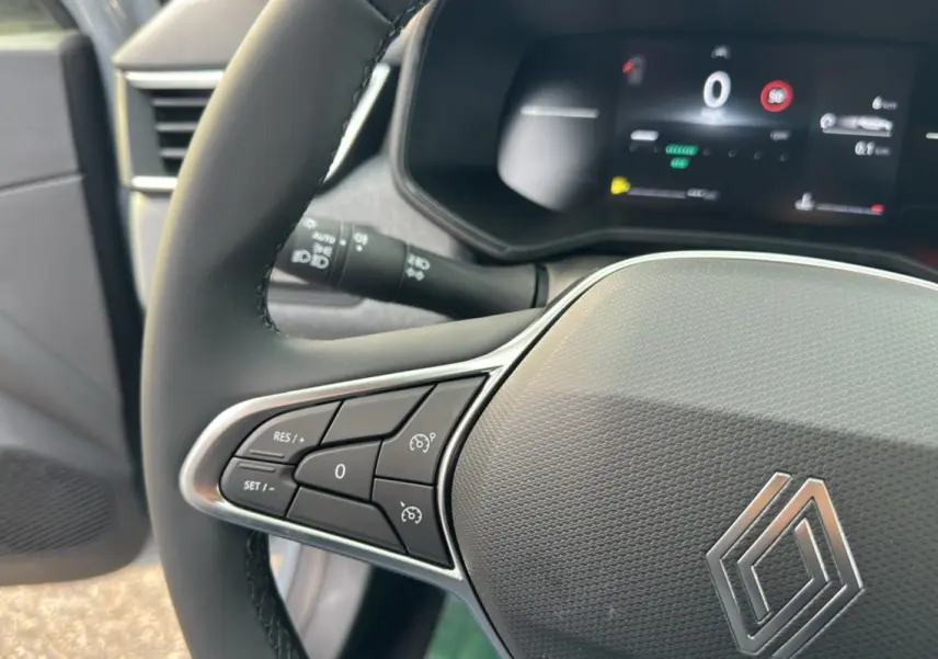 Gros plan sur le volant cuir multifonctions de la Renault Clio DCI 100 Evolution, tableau de bord numérique en arrière-plan.