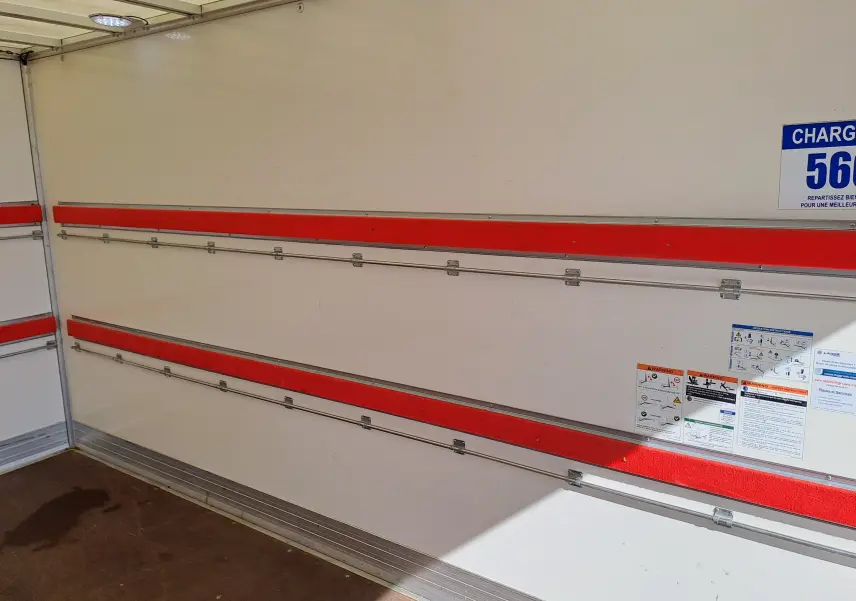 Intérieur du coffre blanc du Nissan Interstar Châssis Cabine 2024, avec barres de fixation rouges et panneaux d'avertissement.