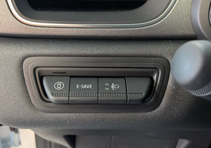 Gros plan sur les boutons de commande E-SAVE et réglage des phares dans l'habitacle du Renault Captur blanc nacré 2025.