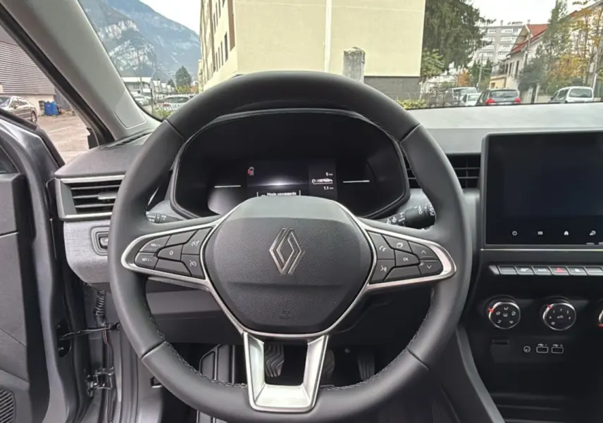 Vue intérieure centrée sur le volant cuir multifonctions d’une Renault Clio gris schiste avec tableau de bord et écran tactile.