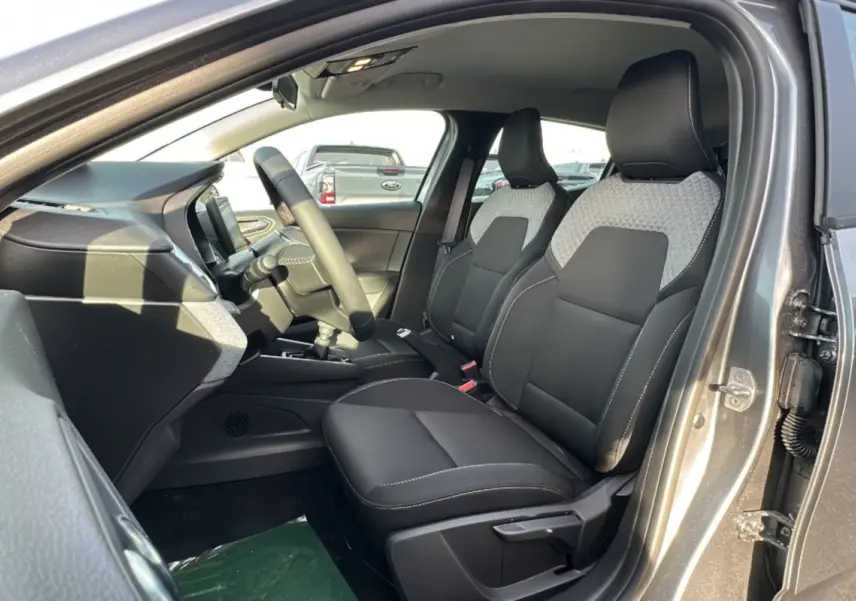 Vue intérieure côté conducteur de la Renault Clio gris schiste 2025, sièges avant bi-matière avec surpiqûres blanches.