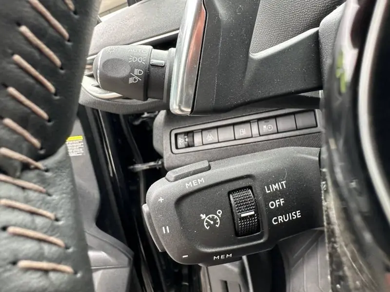 Gros plan sur la commande de régulateur de vitesse côté gauche du volant cuir noir du Peugeot 3008 Hybride 2024.