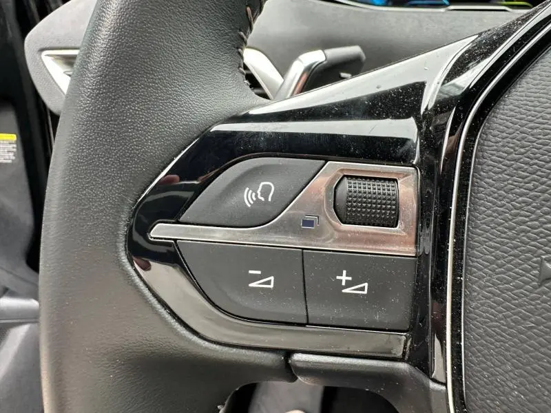 Gros plan sur les commandes gauche du volant cuir noir du Peugeot 3008 Hybride Rechargeable 2024, avec boutons de volume et commande vocale.